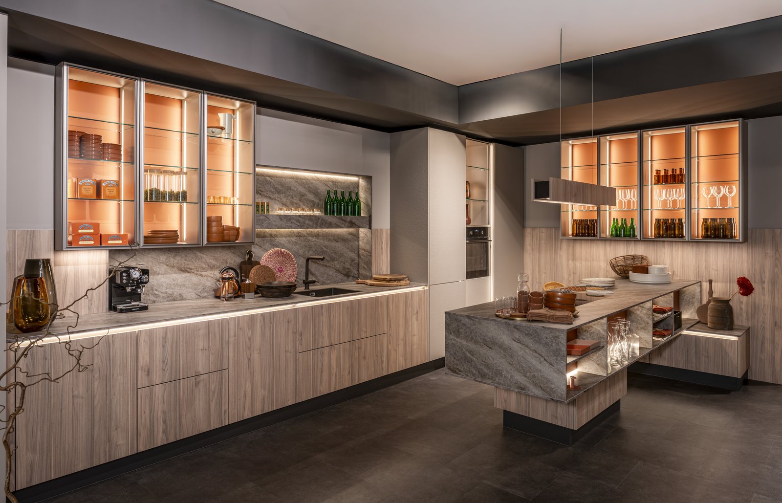 Cuisine contemporaine avec îlot central, façades en bois et vitrines éclairées.